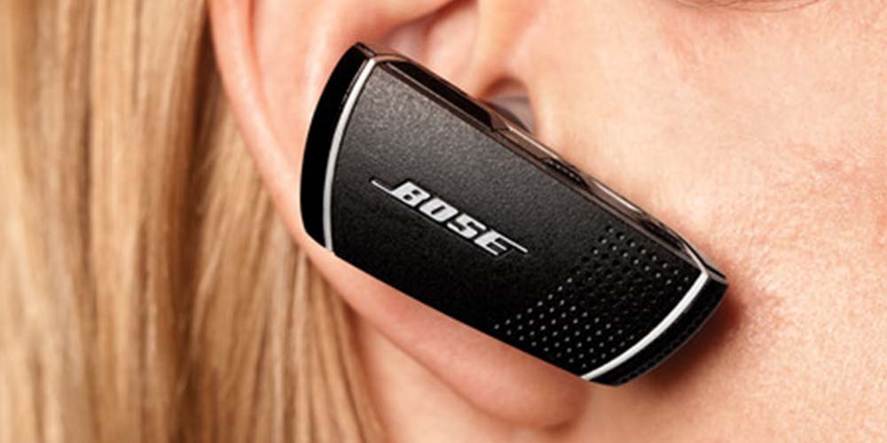 A Bose brand earphone in a blonde woman's ear, close-up. 